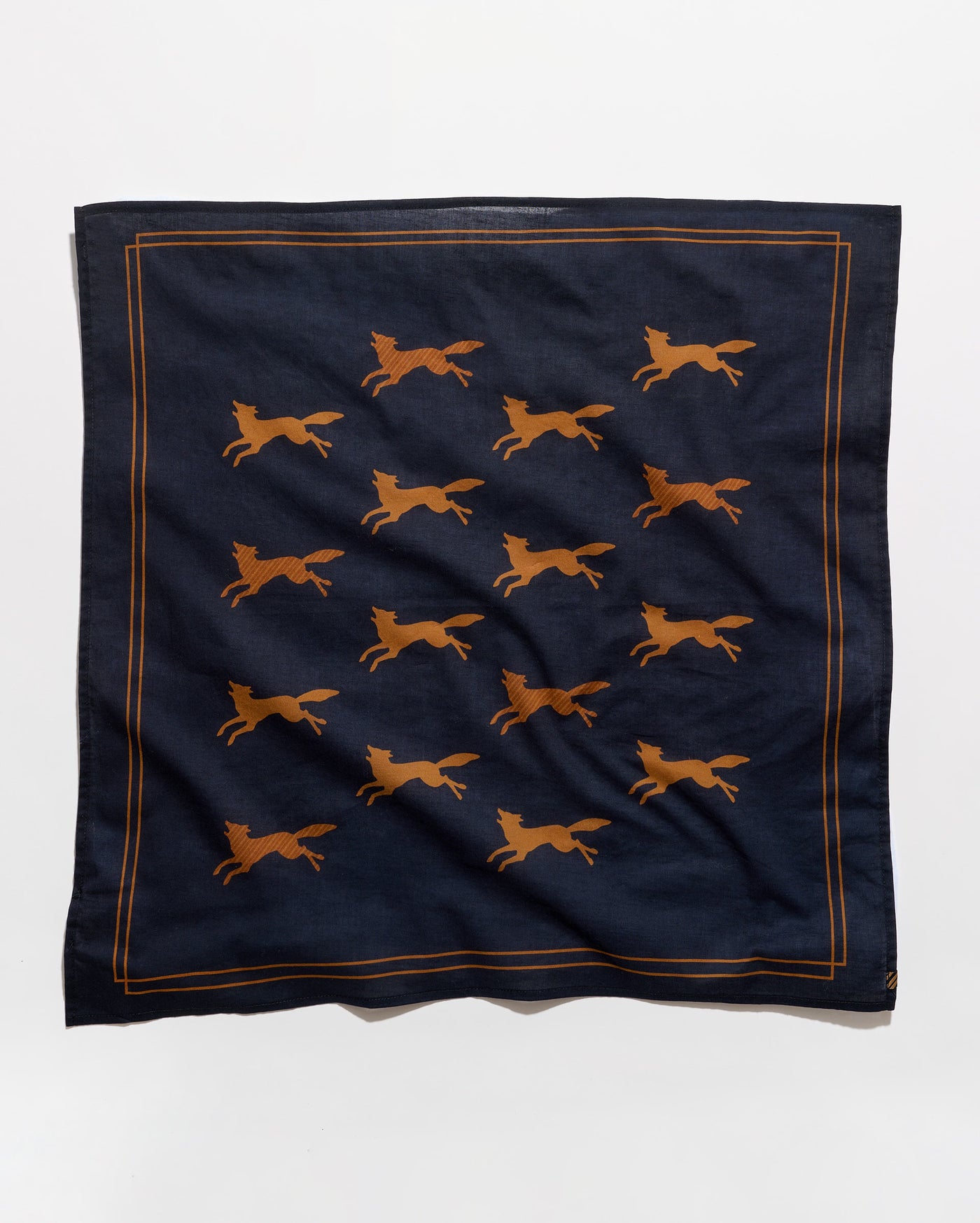 A square navy blue scarf featuring a repeating pattern of running foxes in a warm orange-brown color, framed by a thin orange-brown border line, shown against a plain white background.