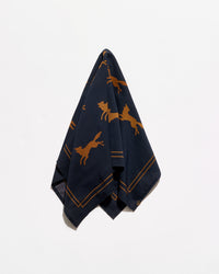 A navy blue silk scarf with a pattern of golden-brown leaping foxes and double-line borders, photographed against a clean white background.