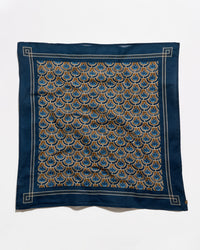 A square silk scarf featuring a navy blue border and a central pattern of repeating fan-shaped motifs in blue, gold, and beige, laid flat against a white background.