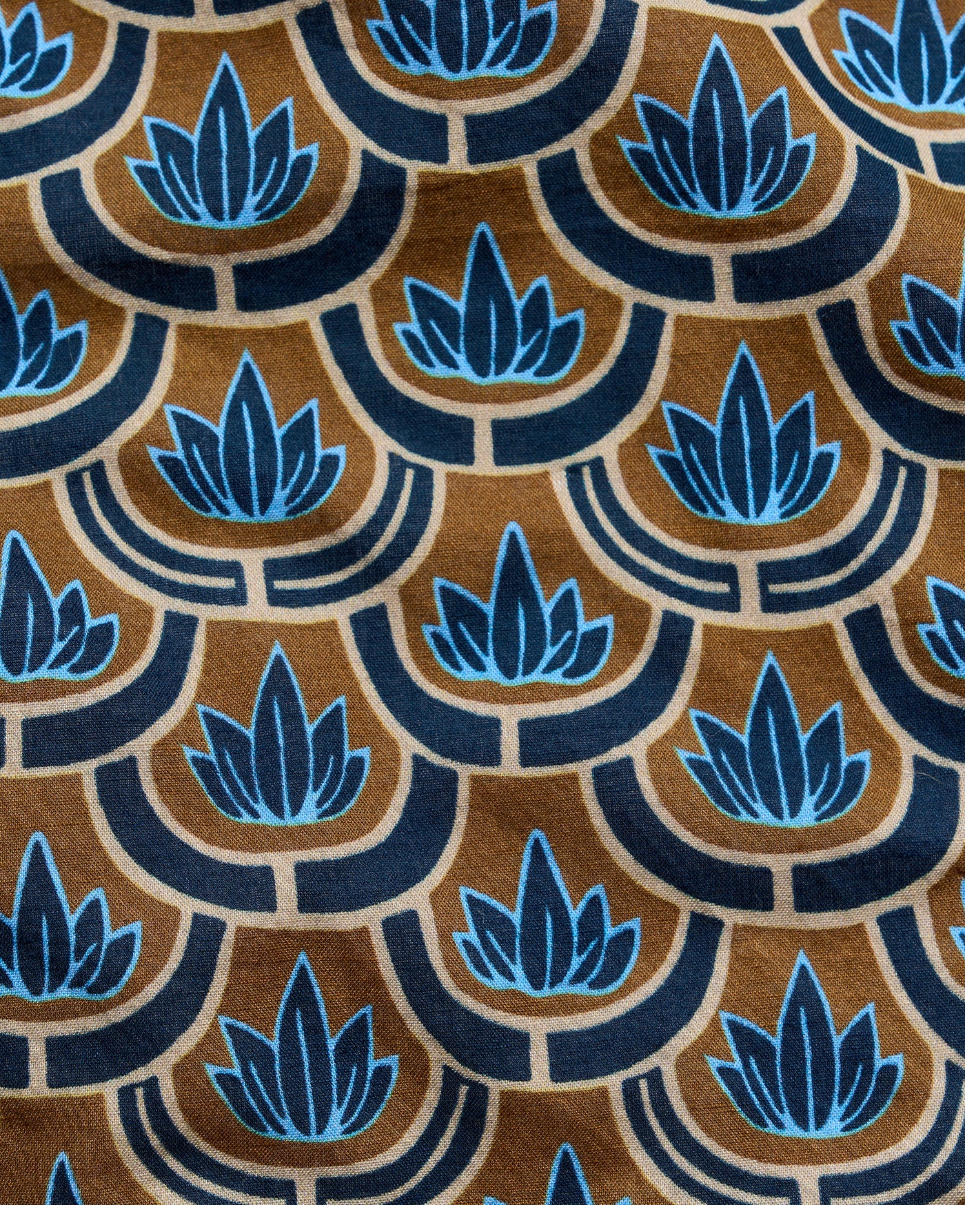 A close-up of a patterned fabric featuring a repeating Art Deco style design with blue lotus flowers and scalloped arches on a warm brown background.