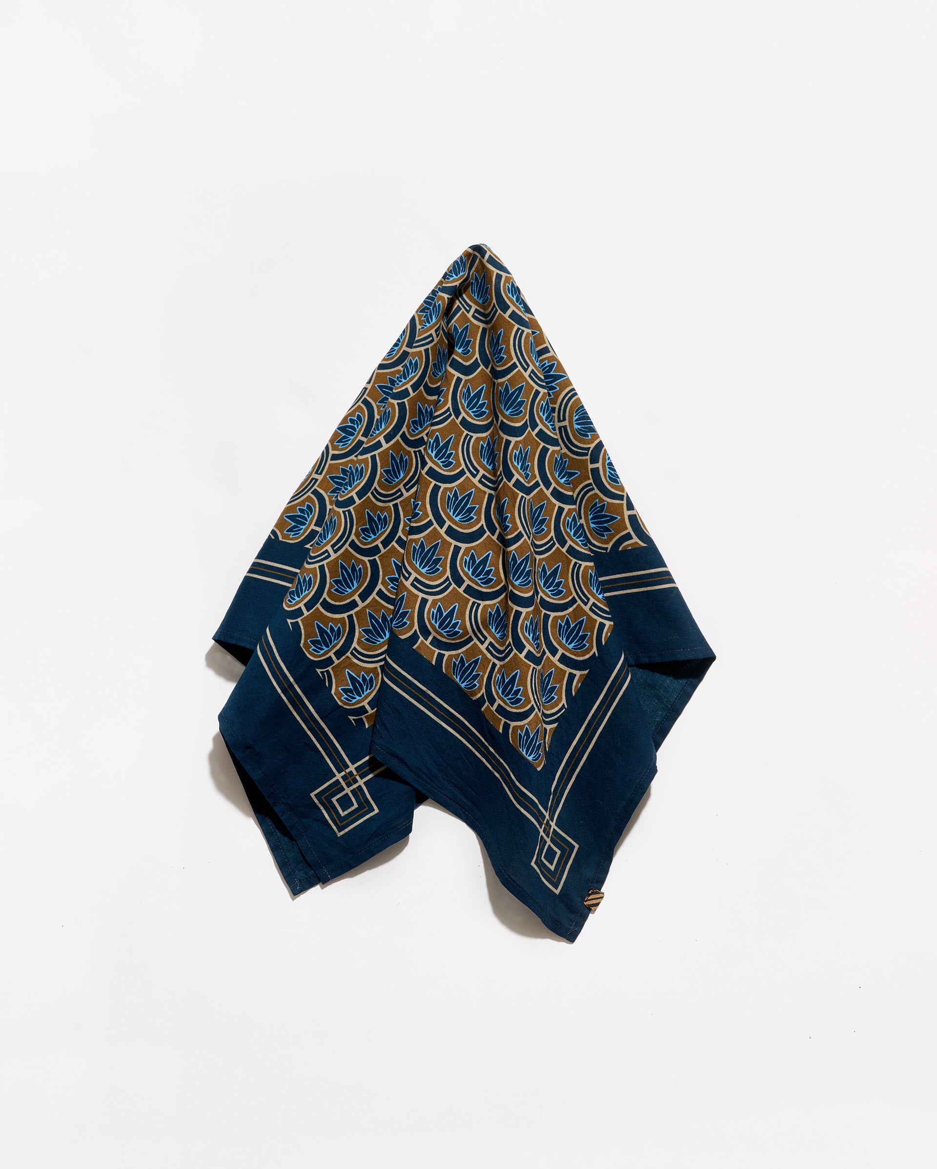 A folded navy blue silk scarf with a gold and teal peacock feather pattern and white geometric borders, displayed on a clean white background.