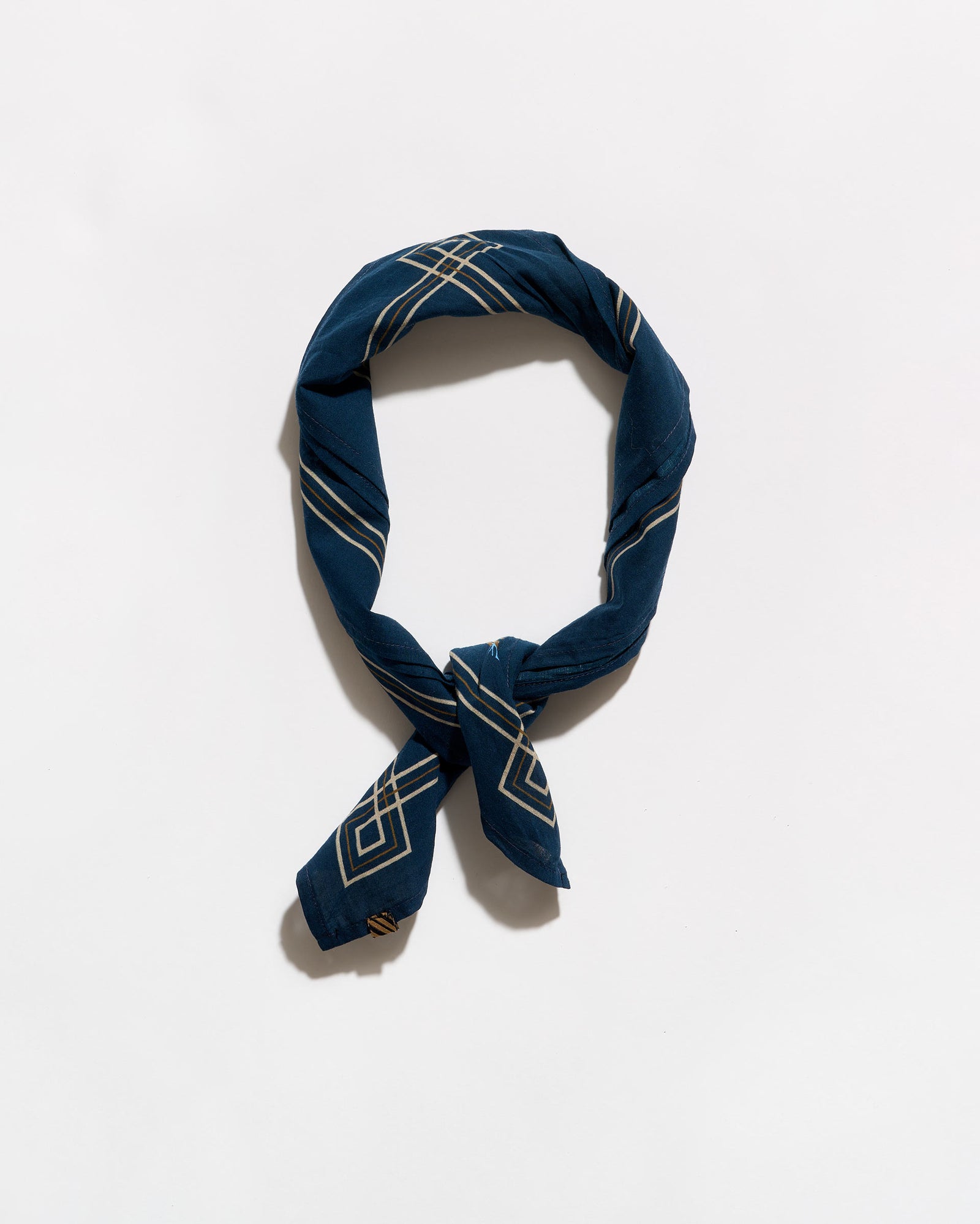 A navy blue silk scarf with a white geometric pattern, tied in a loop and knot, displayed on a clean white background.