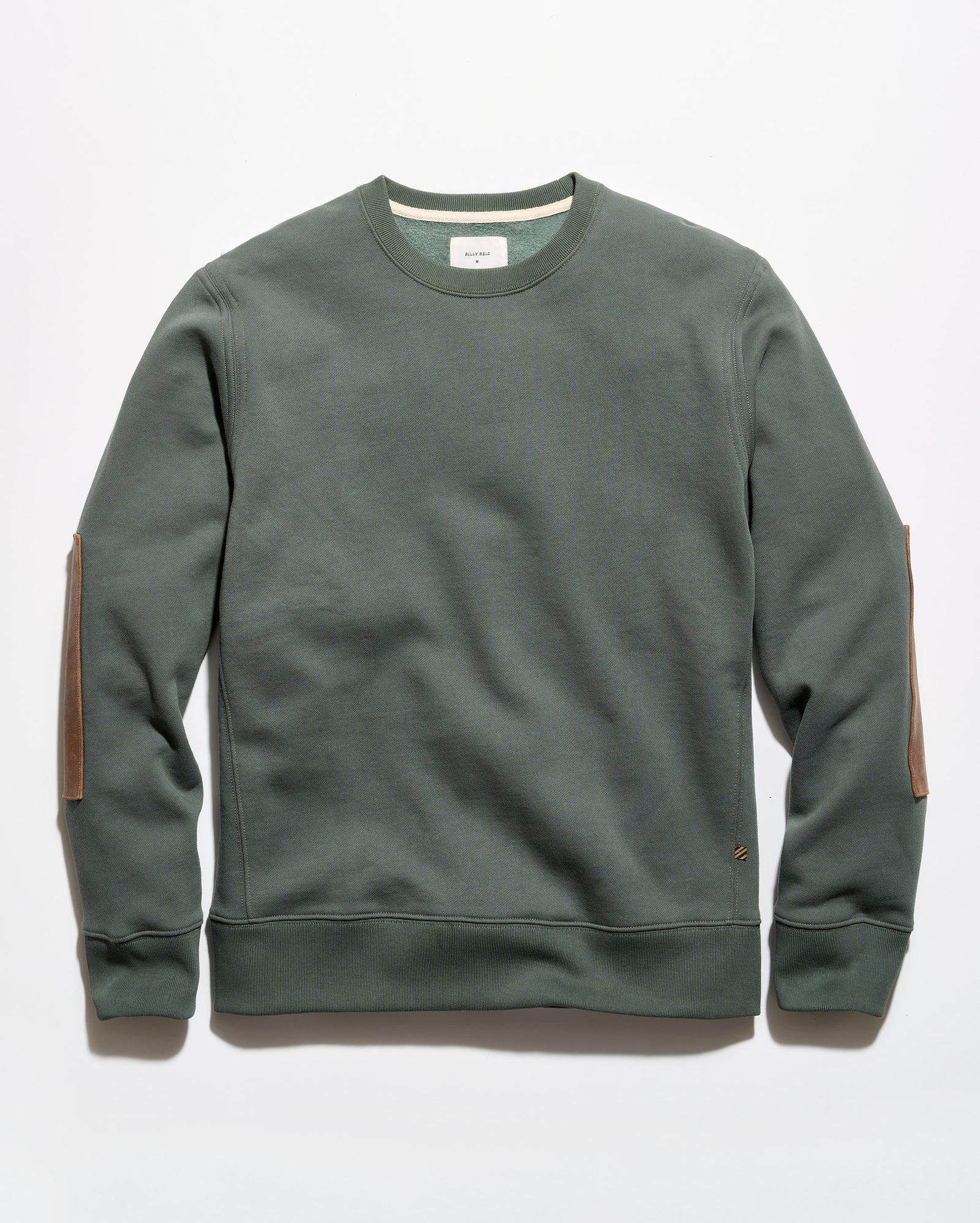 An olive green crewneck sweatshirt with brown leather elbow patches, laid flat against a light gray background.