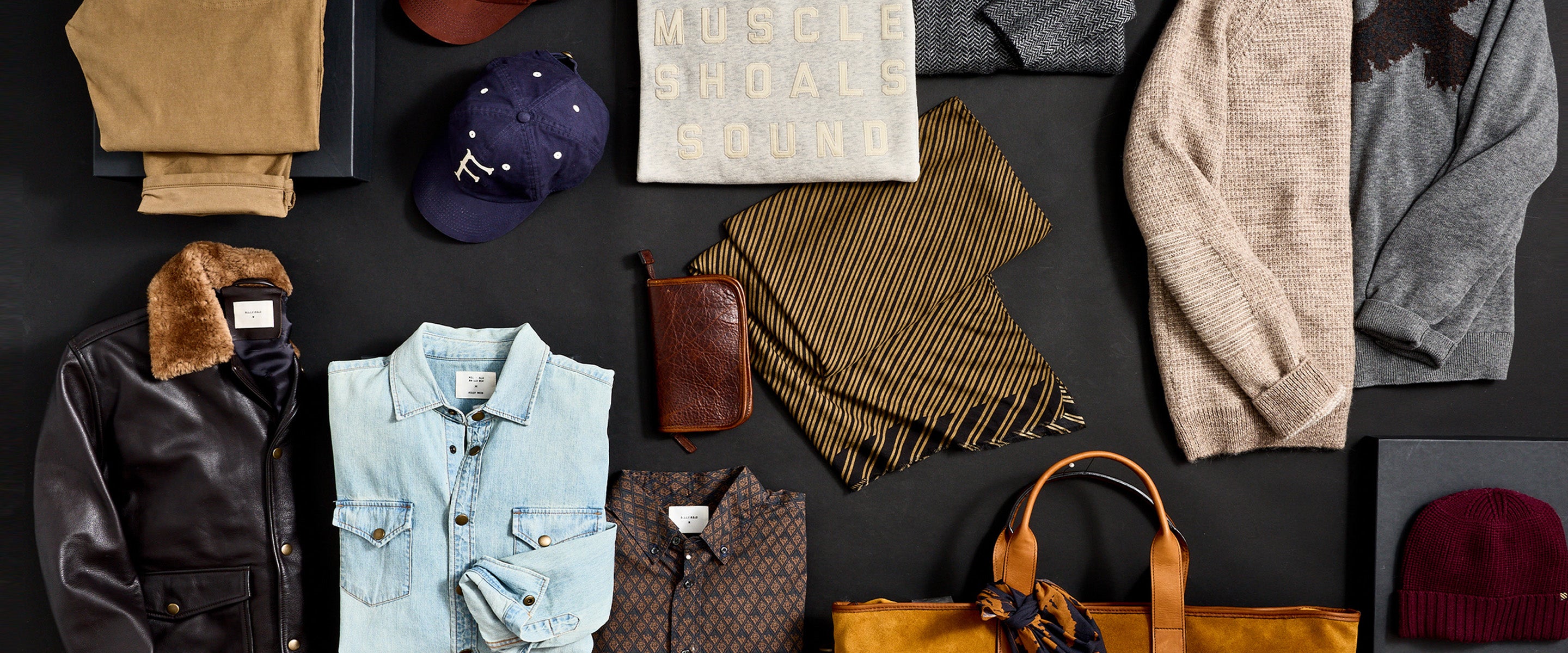 Men's casual clothing and accessories arranged on a dark surface.