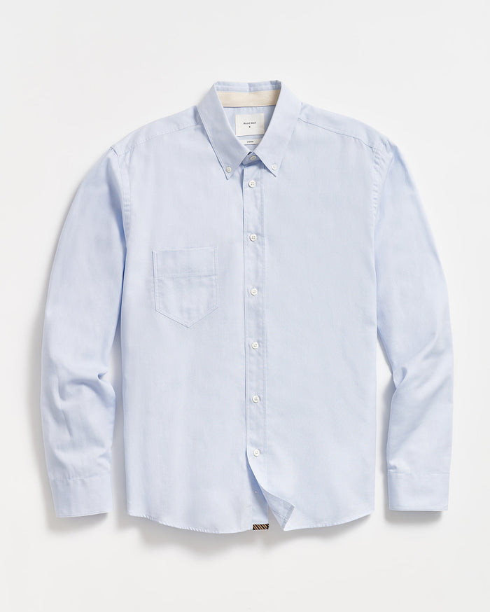 A light blue, long-sleeve button-down shirt with a single chest pocket, buttoned collar, and white buttons, laid flat on a white background.