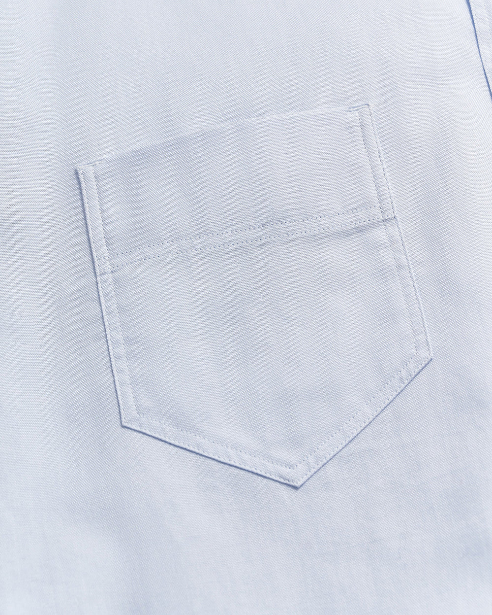 Close-up of a light blue fabric with a single, neatly stitched chest pocket visible in the center of the image.