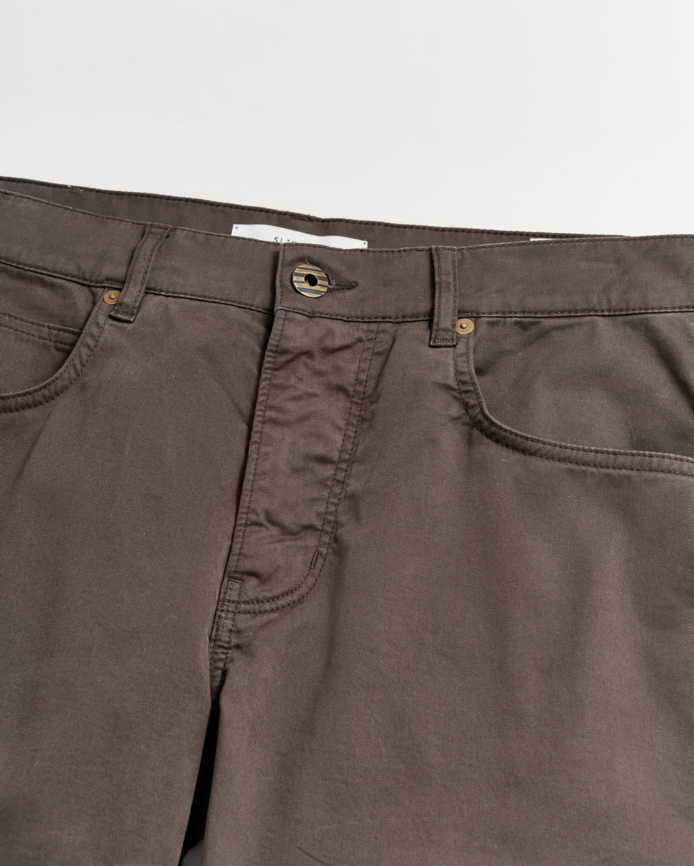 A close-up view of the waistband and upper section of brown pants with visible pockets, belt loops, and a button closure against a white background.