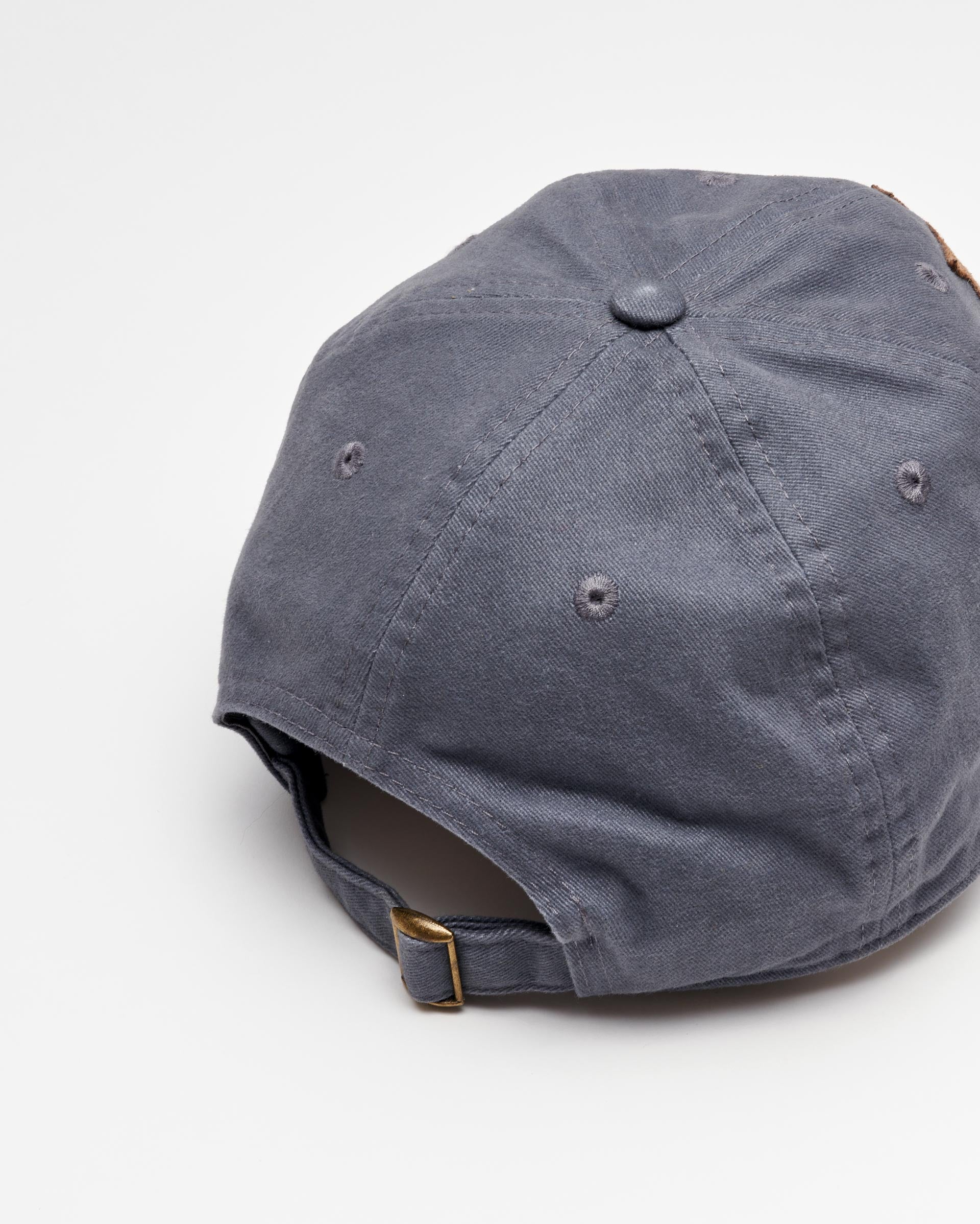 A gray baseball cap viewed from the back, showing a fabric strap with a metal buckle for size adjustment. The cap is placed on a white surface.