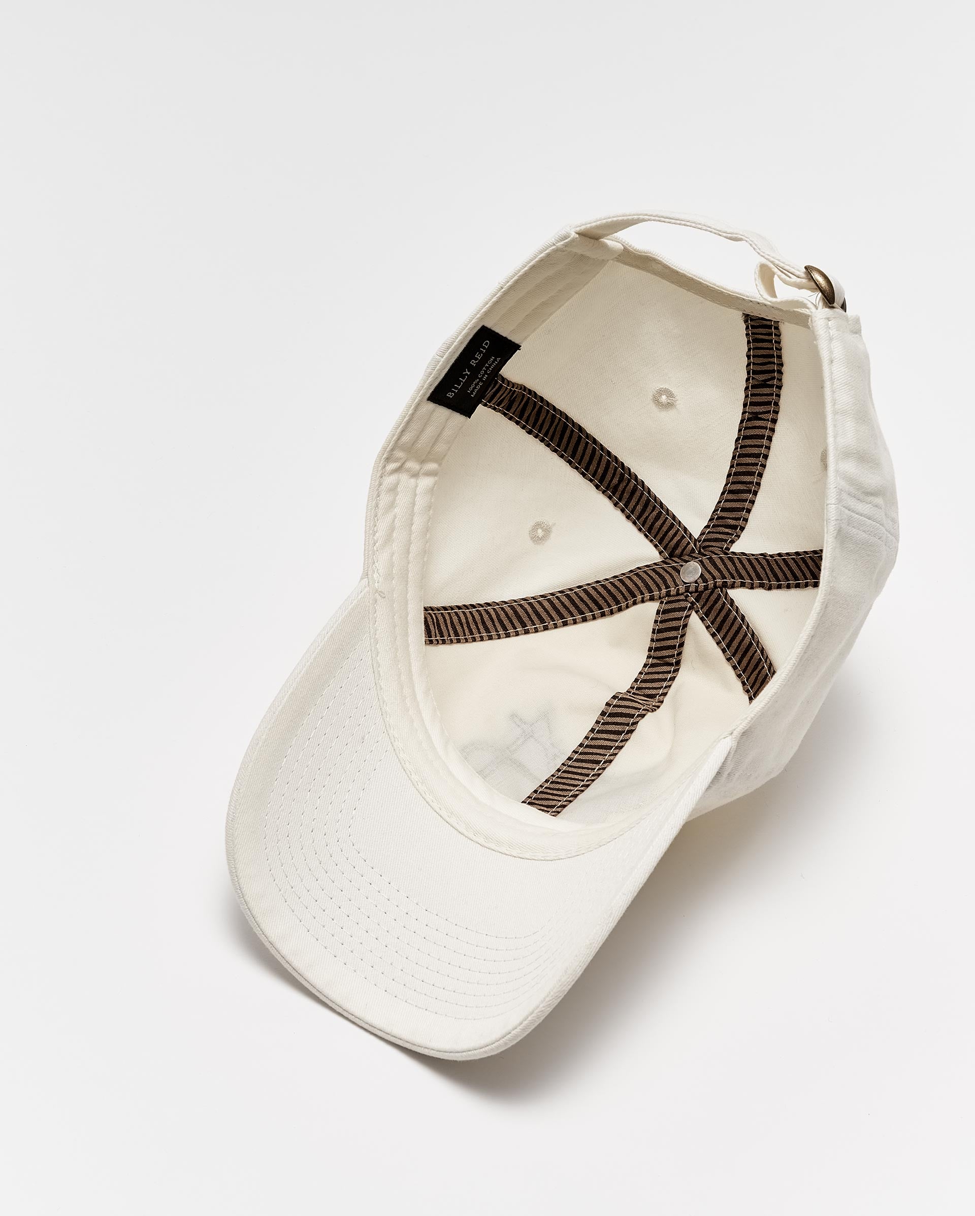 An upside-down white baseball cap with visible brown stitching on the inside, a black label, and an adjustable strap, displayed on a white background.