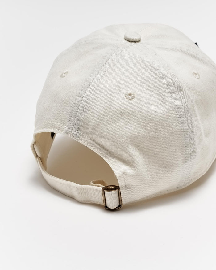 A beige baseball cap viewed from the back, showing an adjustable strap with a metal buckle and stitched ventilation holes on the crown, set against a white background.