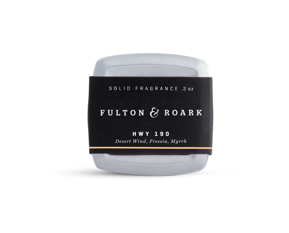 A rectangular metal tin of Fulton & Roark solid fragrance, HWY 190, with a black label featuring the scents Desert Wind, Freesia, and Myrrh. The tin is placed against a plain white background.