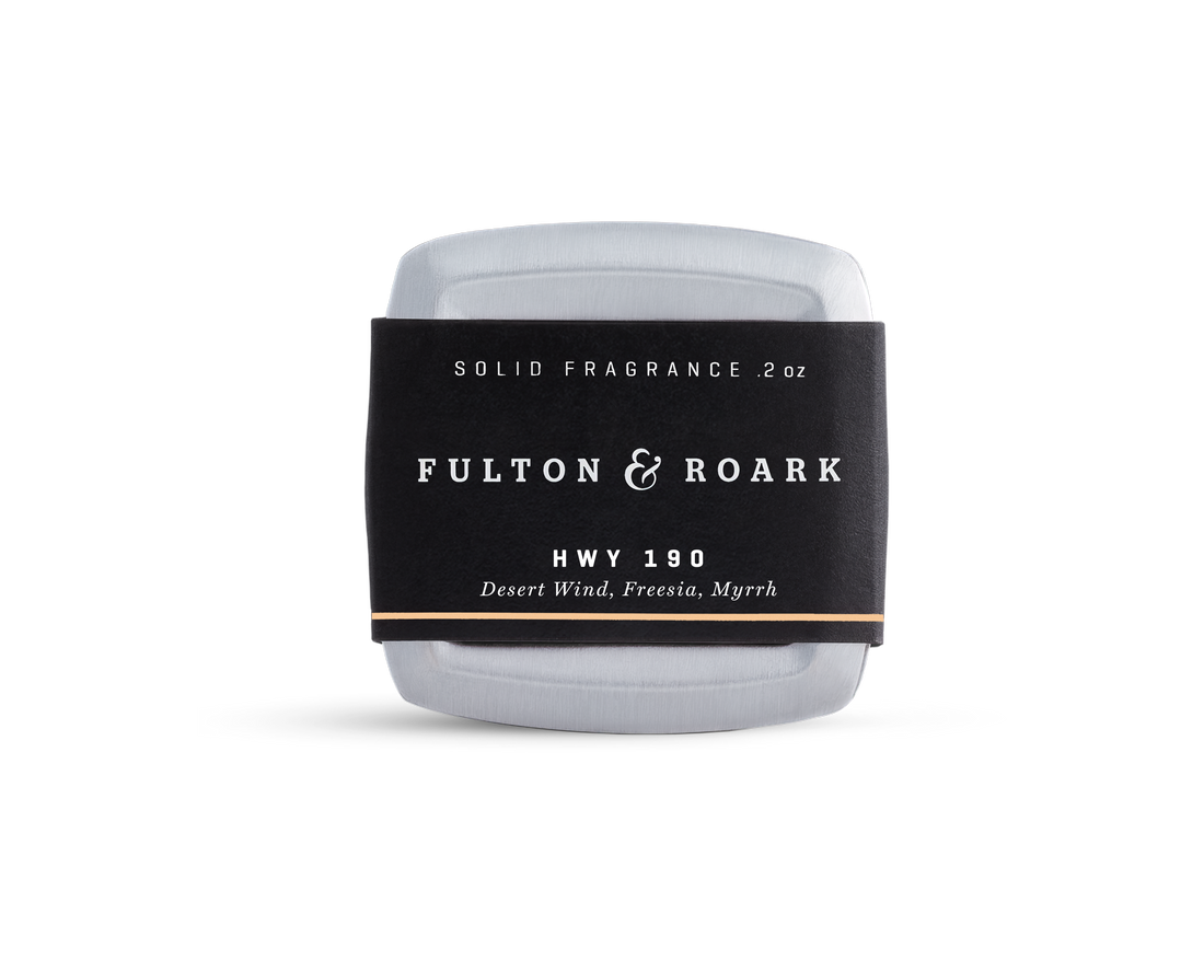 A rectangular metal tin of Fulton & Roark solid fragrance, HWY 190, with a black label featuring the scents Desert Wind, Freesia, and Myrrh. The tin is placed against a plain white background.