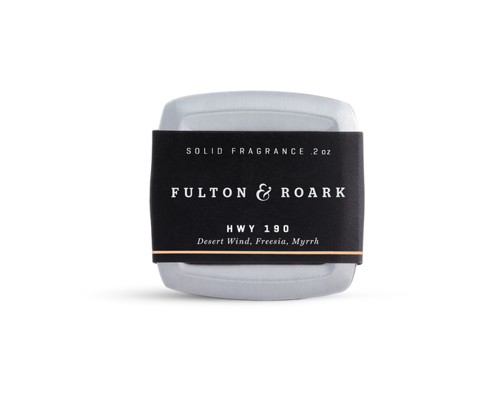 A rectangular metal tin of Fulton & Roark solid fragrance, HWY 190, with a black label featuring the scents Desert Wind, Freesia, and Myrrh. The tin is placed against a plain white background.