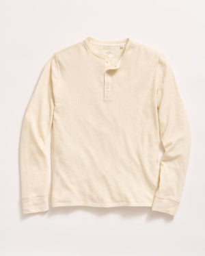 A long-sleeve, cream-colored henley shirt with a round neckline and three buttons down the front, laid flat on a white background.