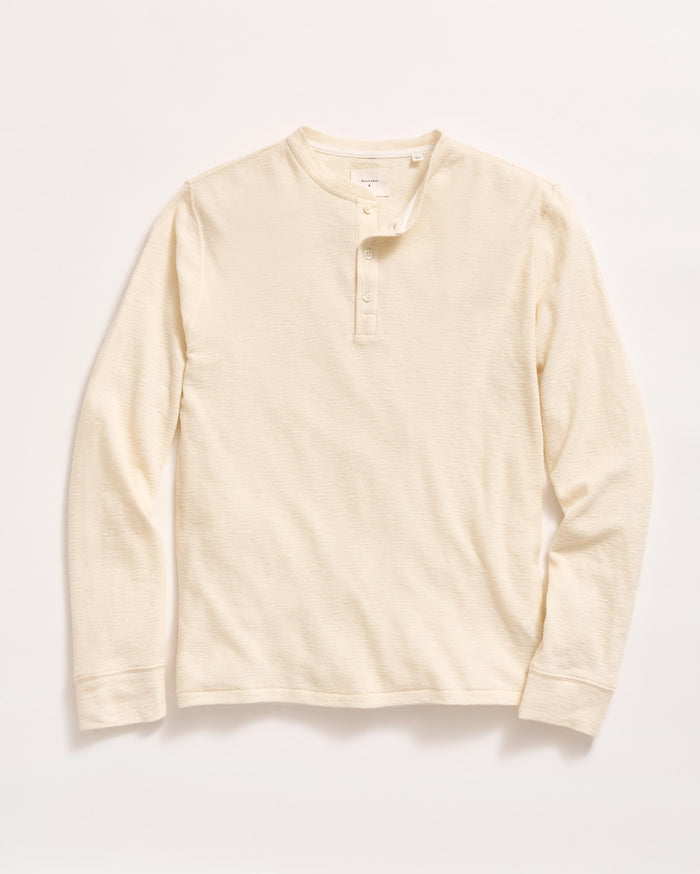 A long-sleeve, cream-colored henley shirt with a round neckline and three buttons down the front, laid flat on a white background.