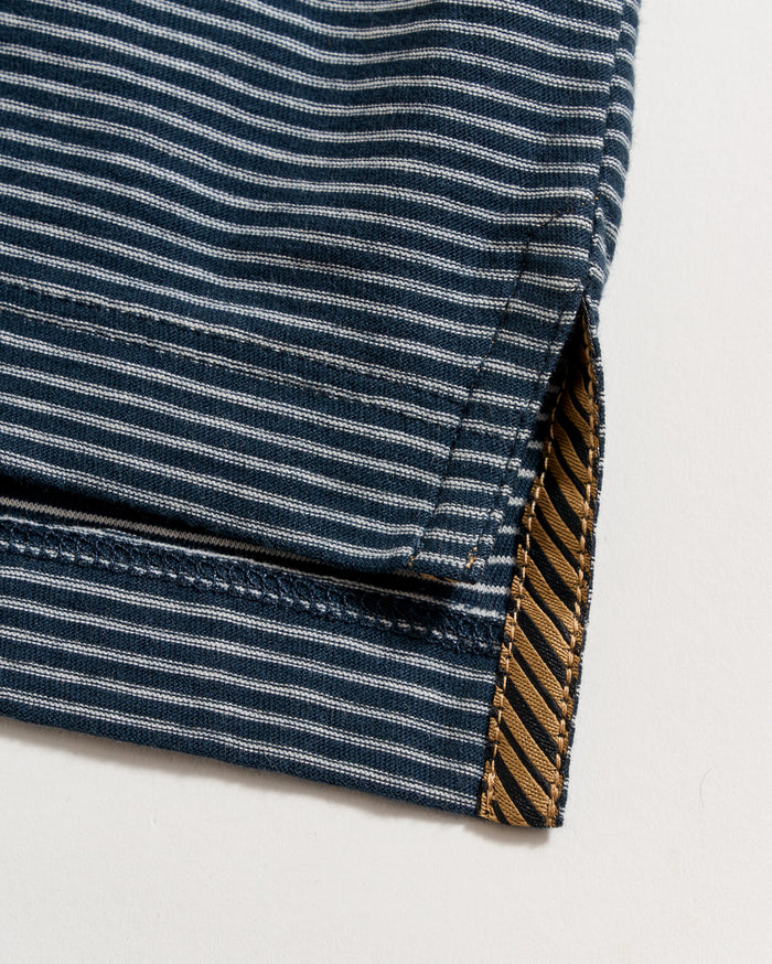 Close-up of a blue and white striped fabric edge with detailed stitching and a small side slit, revealing a contrasting brown and black diagonal striped inner fabric.