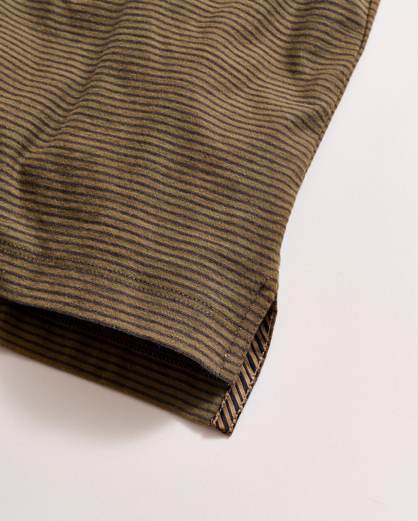 A close-up of the hem of a brown and black striped fabric, possibly a shirt or sleeve, set against a light background. The stripes run horizontally, and the stitching is visible at the edge.