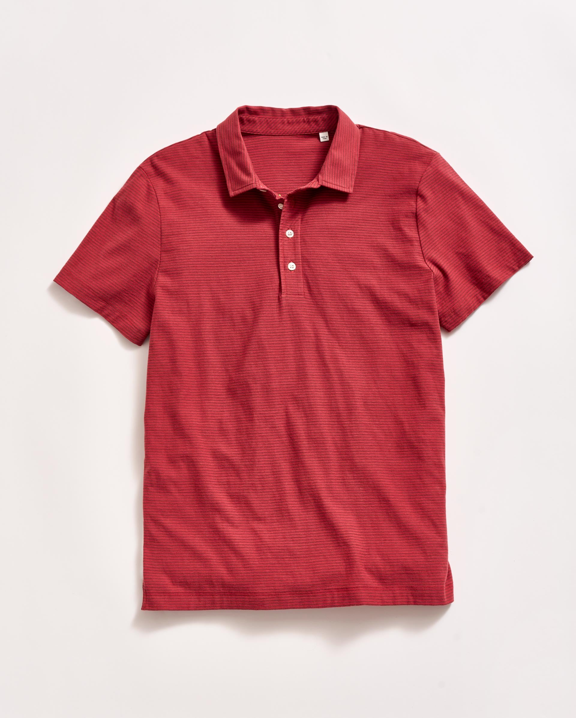 A short-sleeve, red polo shirt with a collar and three white buttons, laid flat on a white background.