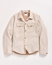 A beige, long-sleeve button-up shirt with two chest pockets and brown buttons, laid flat on a white background.