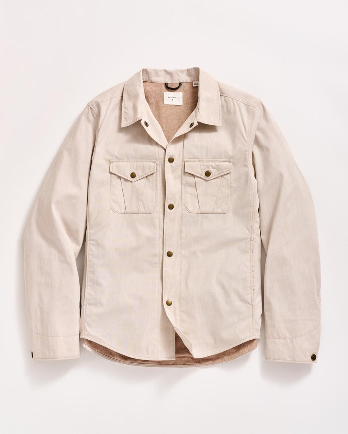 A beige, long-sleeve button-up shirt with two chest pockets and brown buttons, laid flat on a white background.