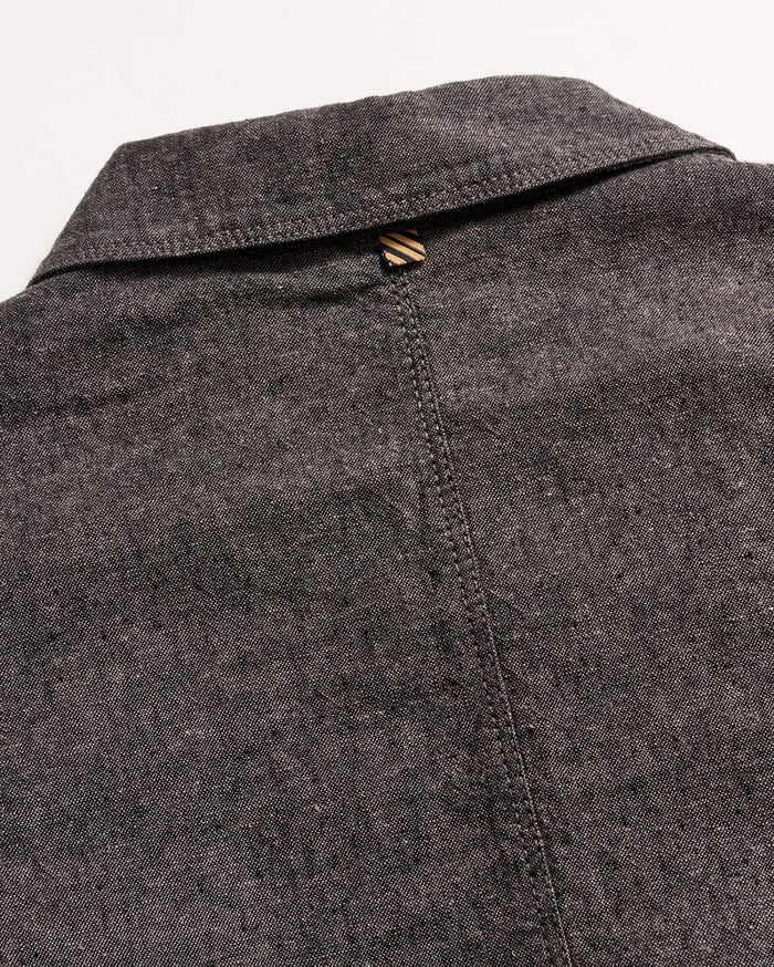Close-up of the back of a grey textured collared shirt, showing a seam running down the center and a small brown and beige striped loop at the top below the collar.