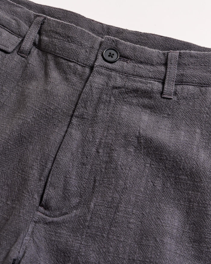 Close-up of the waistband and upper section of a pair of gray textured pants with a button closure and belt loops, set against a light background.