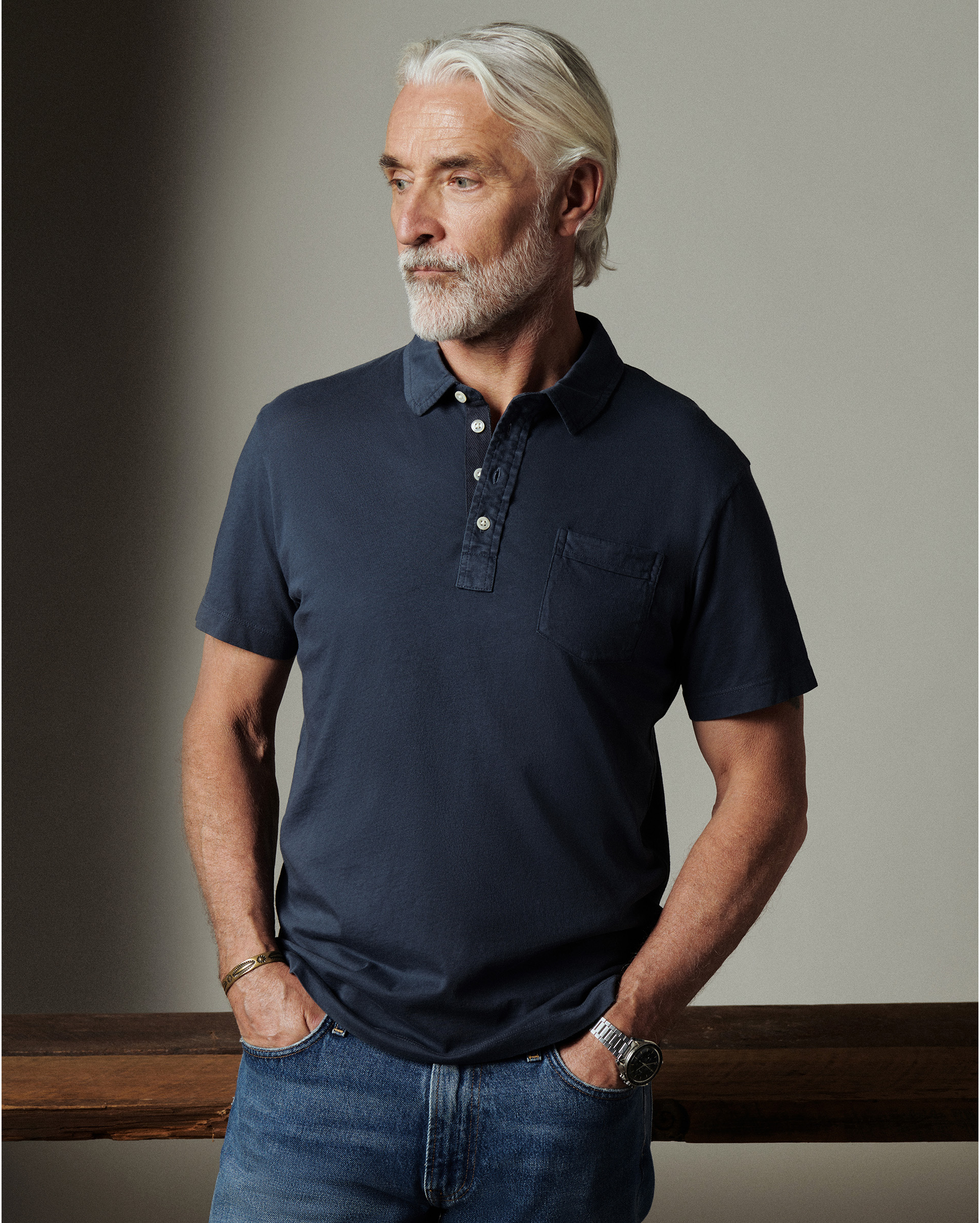 Man wearing a navy polo shirt and jeans against a neutral background