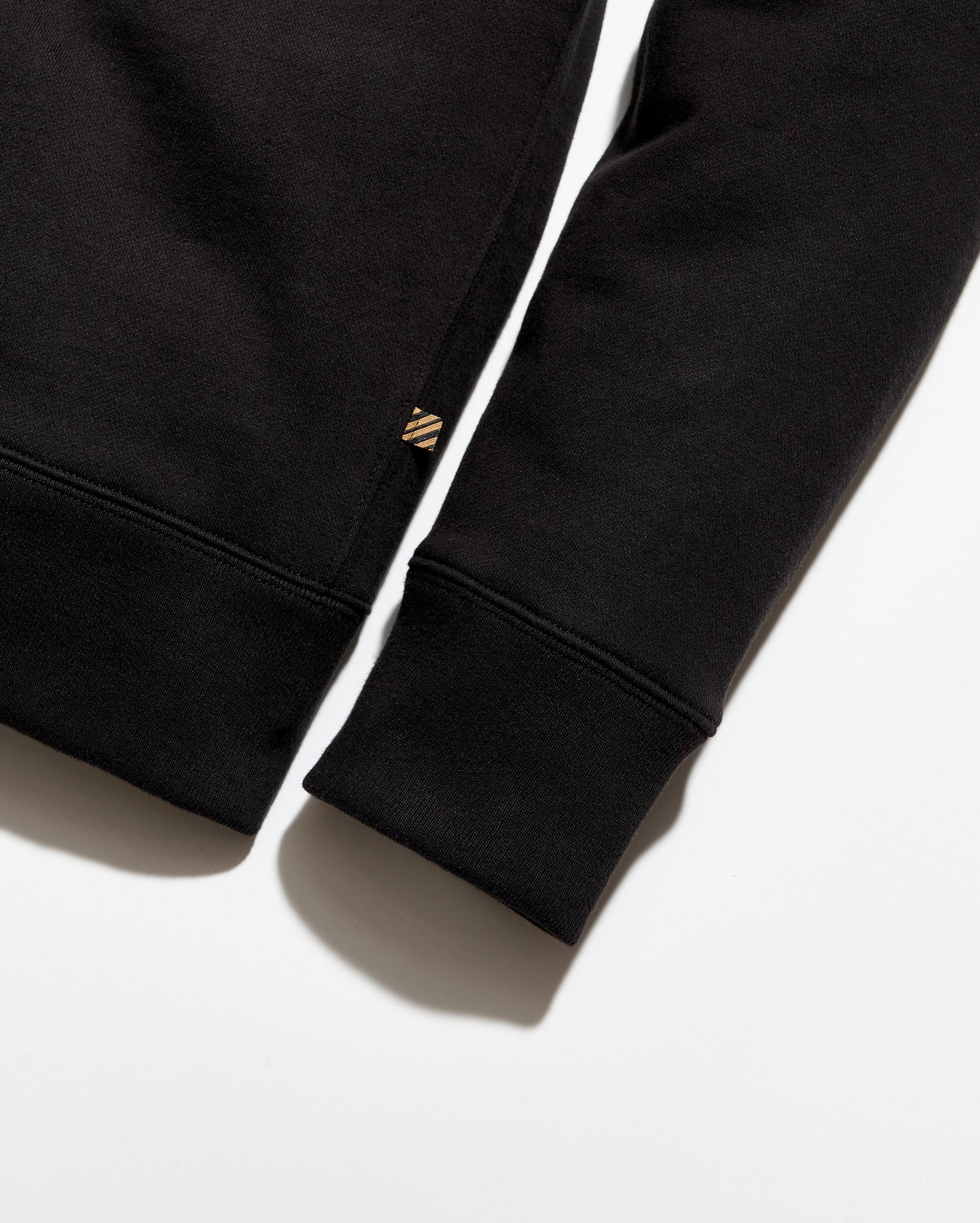 Close-up of a black sweatshirt with a brand logo on the sleeve against a white background