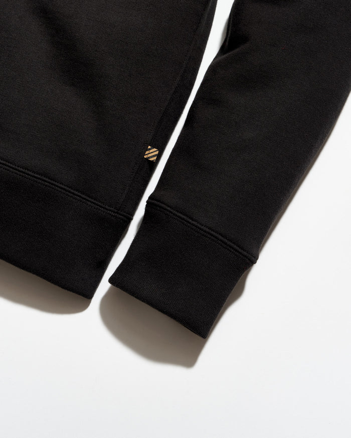 Close-up of a black sweatshirt with a brand logo on the sleeve against a white background