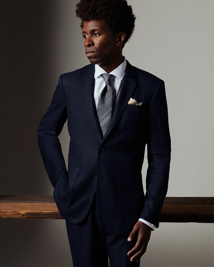 Man wearing a navy suit with a gray tie against a neutral background
