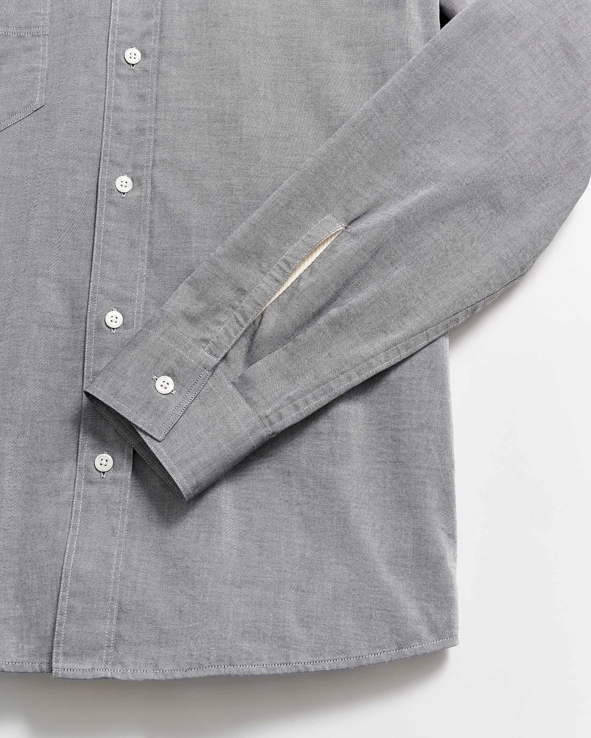 A close-up of a light gray button-up shirt with white buttons, showing the sleeve and part of the shirts front laid flat on a white surface.