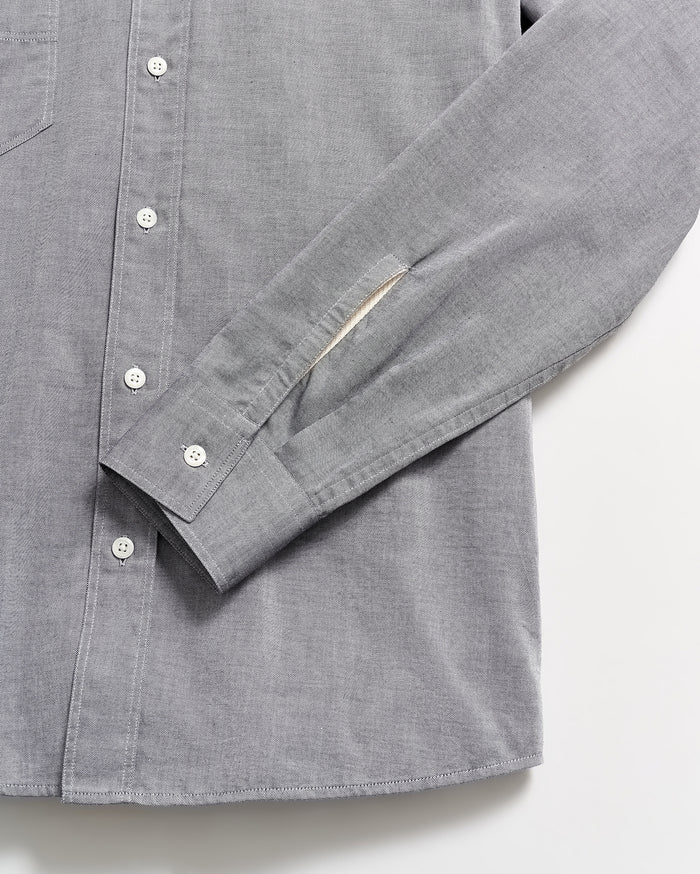 A close-up of a light gray button-up shirt with white buttons, showing the sleeve and part of the shirts front laid flat on a white surface.