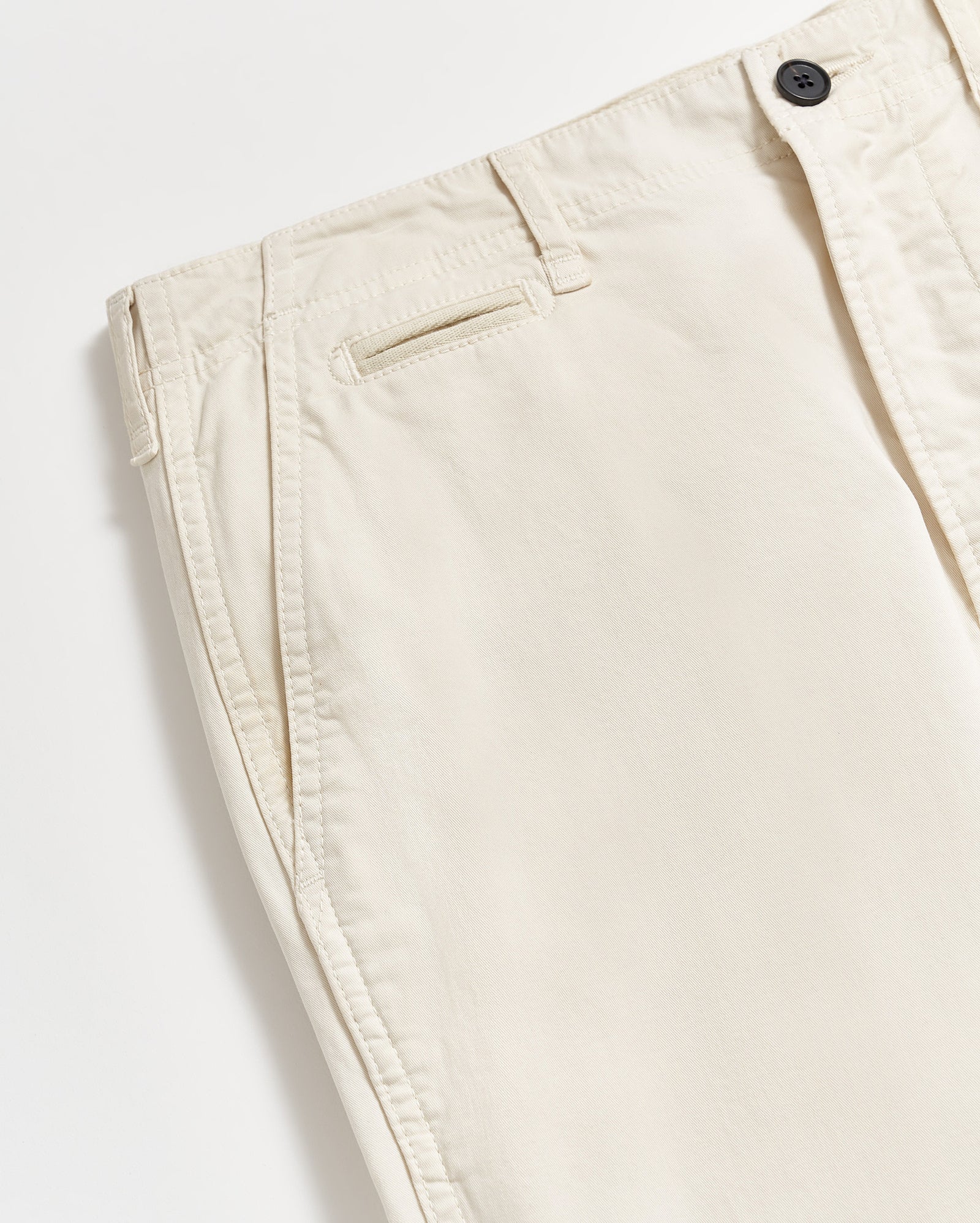 A close-up of a pair of light beige or off-white pants with side pockets, a single back pocket, belt loops, and a visible black button at the waistband. The pants are laid flat on a white surface.