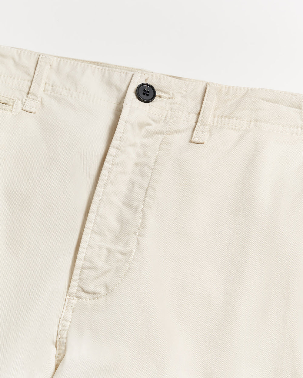 Close-up of a pair of light beige or off-white pants, showing the waistband, belt loops, black button, and part of the fly on a plain white background.
