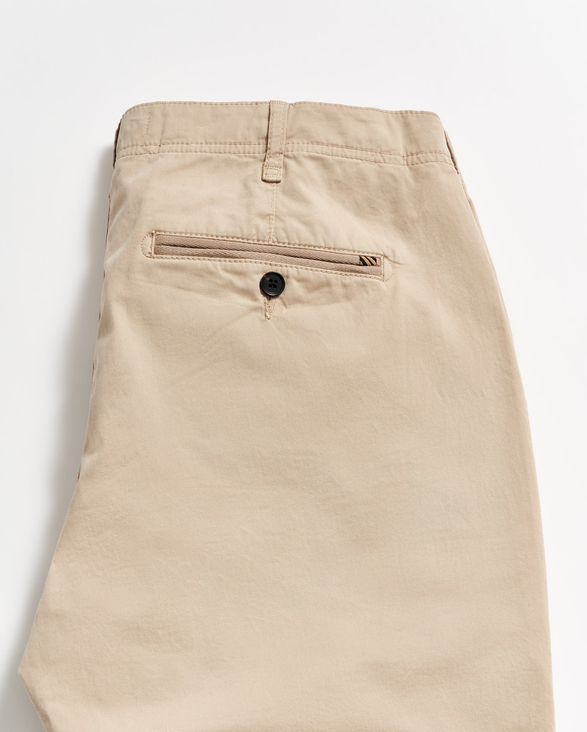 Beige khaki pants folded neatly, showing the back side with a single welt pocket featuring a black button. The fabric appears smooth, and there is a belt loop at the waistband.