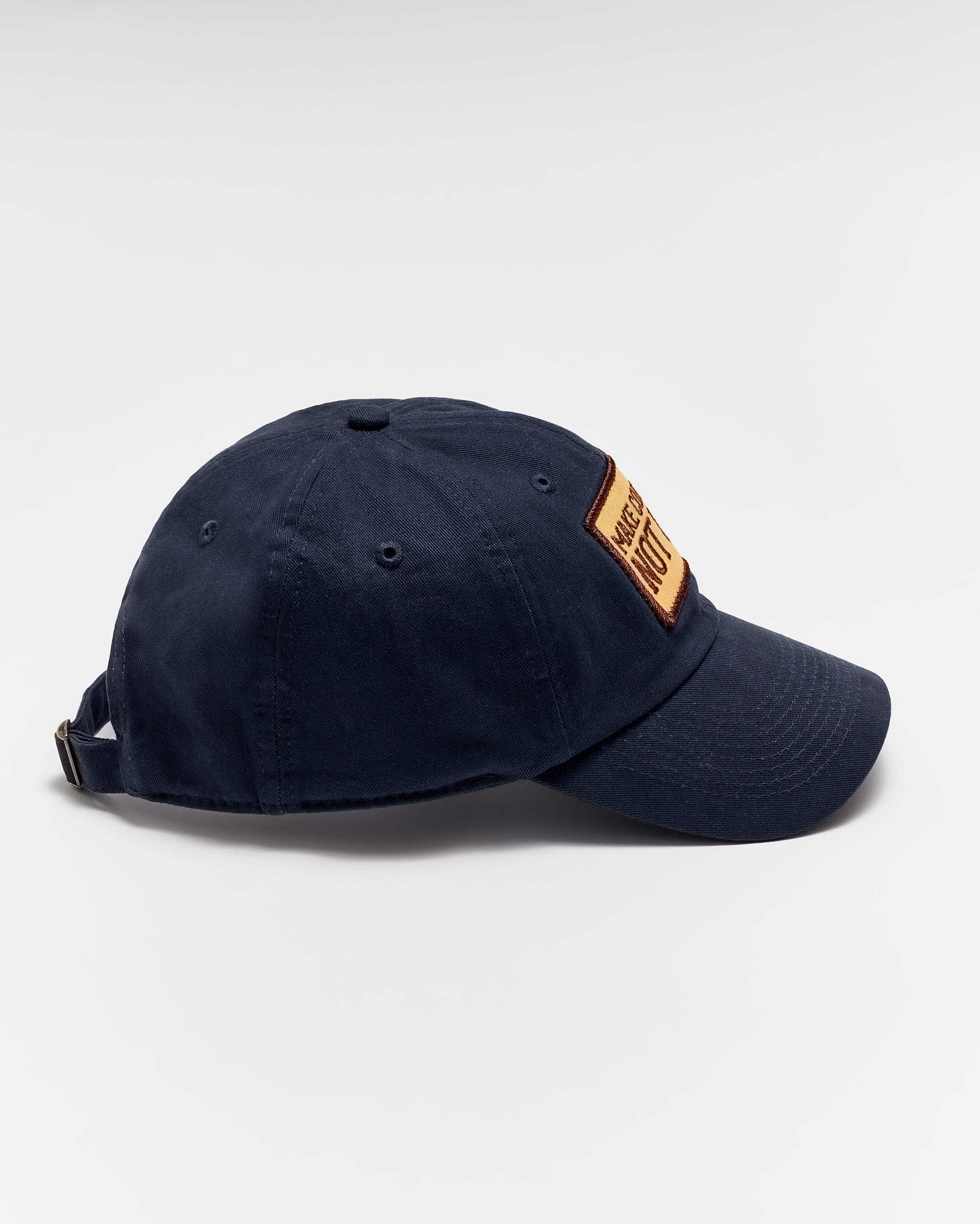 A navy blue baseball cap with a brown rectangular patch on the front, viewed from the side against a plain white background. The cap has an adjustable strap at the back.